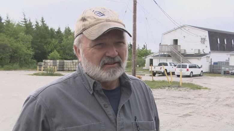 A man stands outside near a large white building and looks off camera.