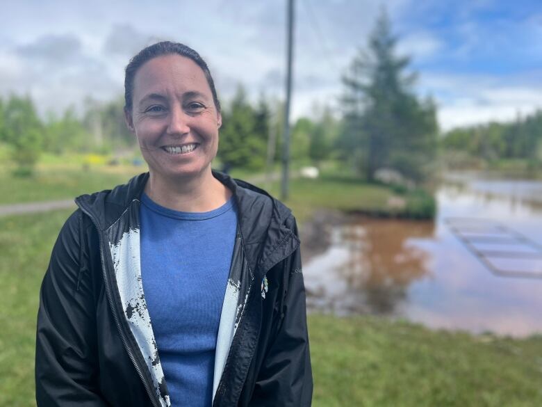 Aleida Tweten stands with her back to a pond. She wears a blue shirt and black rain coat.