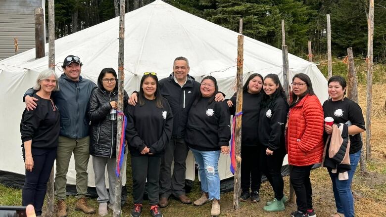 A group of people stand around Innu tent