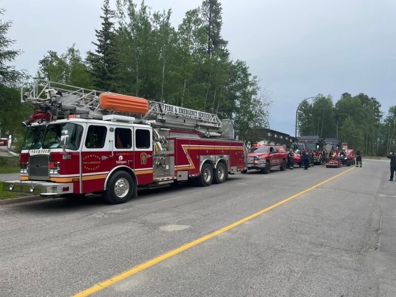 A red fire truck and a number of SUV's lined up along a street.