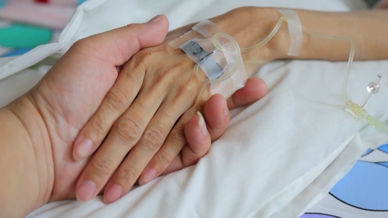 A patient's hand is being held by another person's. An IV can be seen in the patient's hand.