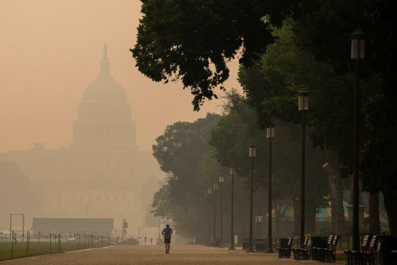 A person is shown at a distance jogging on a path as the U.S. Capitol is shown in the background through a haze.