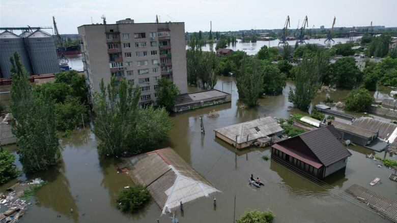 Flooded homes with an apartment building and a river in the background.