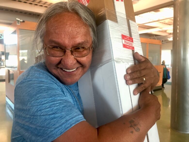 A man in blue shirt hugs a box that contains a 140-year-old robe.