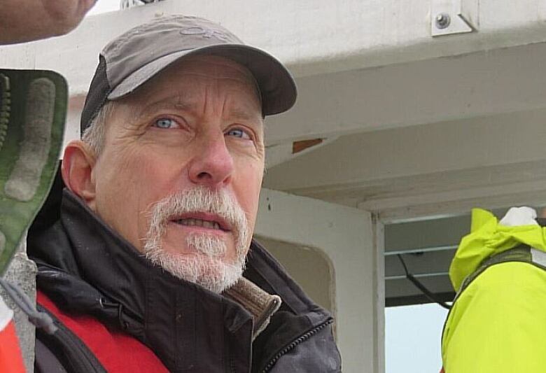 A man in a baseball cap and a heavy coat is seen in closeup on a boat.