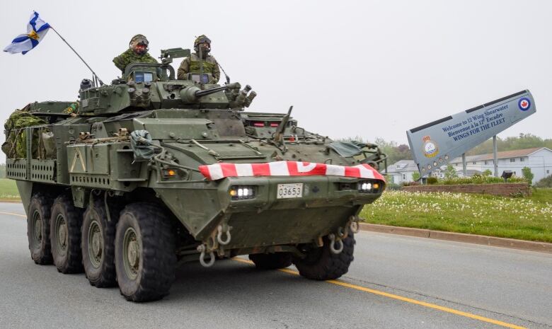 A military tank drives down a road with two uniformed members on top.