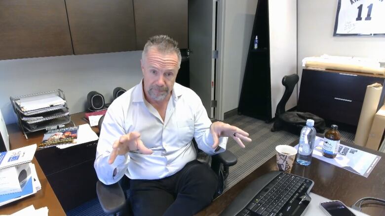 A man is shown in front of a computer in an office speaking on a video call.