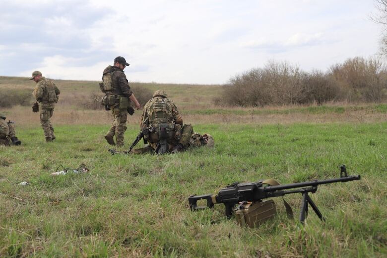 Soldiers do training exercises in a field, with a gun sitting on the ground in the foreground.