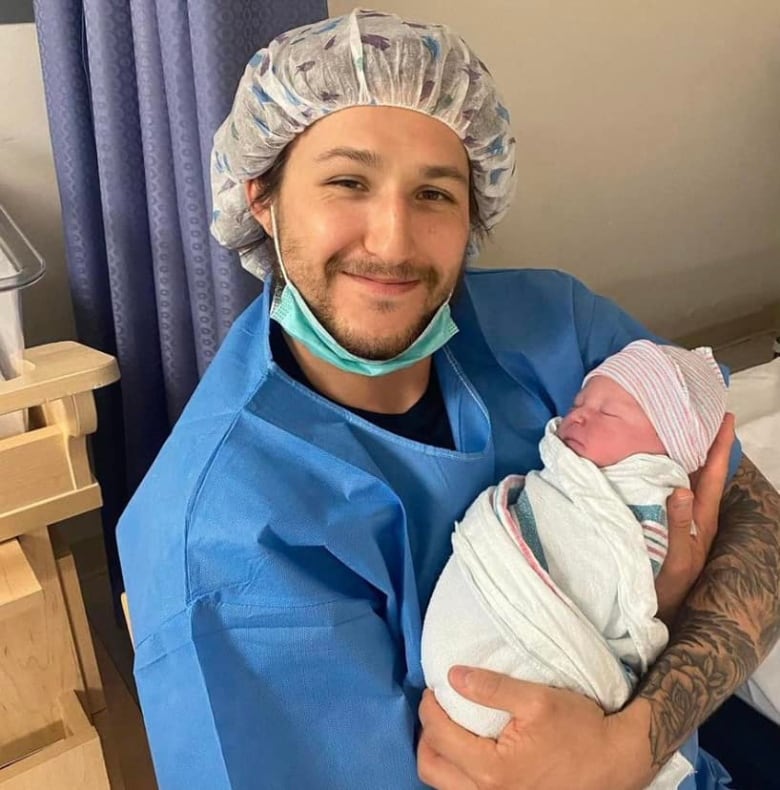 A man in scrubs holding a baby. 