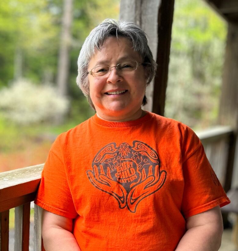 A woman wearing an orange shirt that says 'every child matters' stands on a wooden porch.