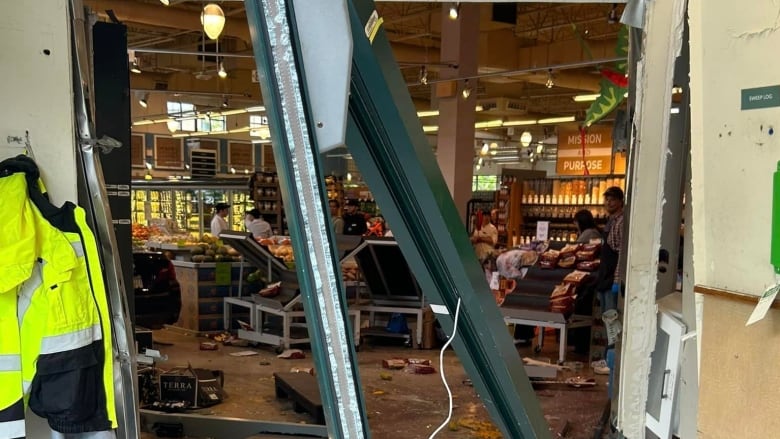 Glass shattered on the ground, and a wall torn down. A car is seen in the corner of a grocery store after it crashed into the building. 