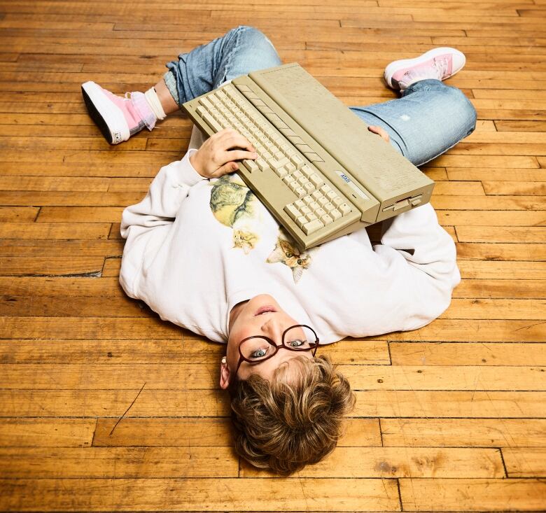 A woman lies on the ground, holding a large device resembling a typewriter.