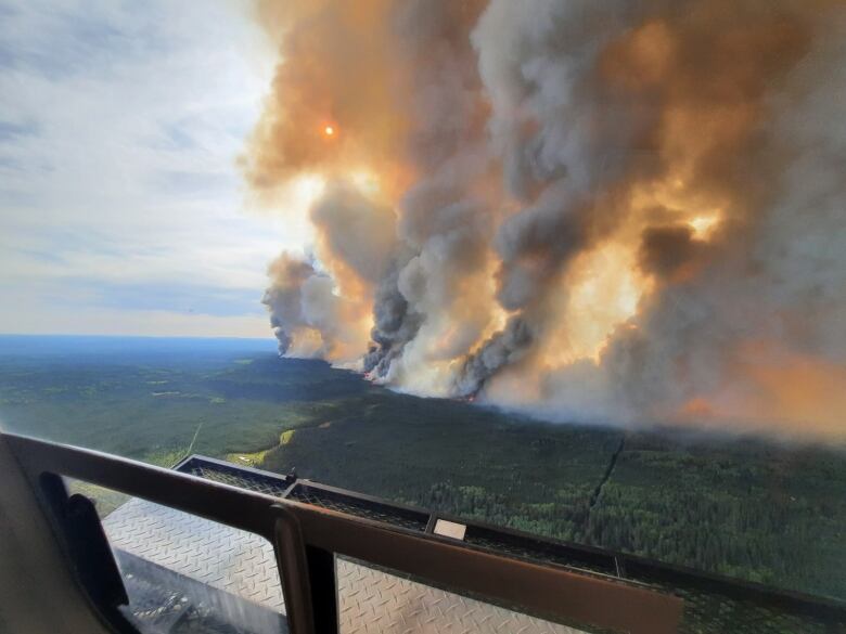 Wide shot of fire and smoke come from a wide area of vegetation.