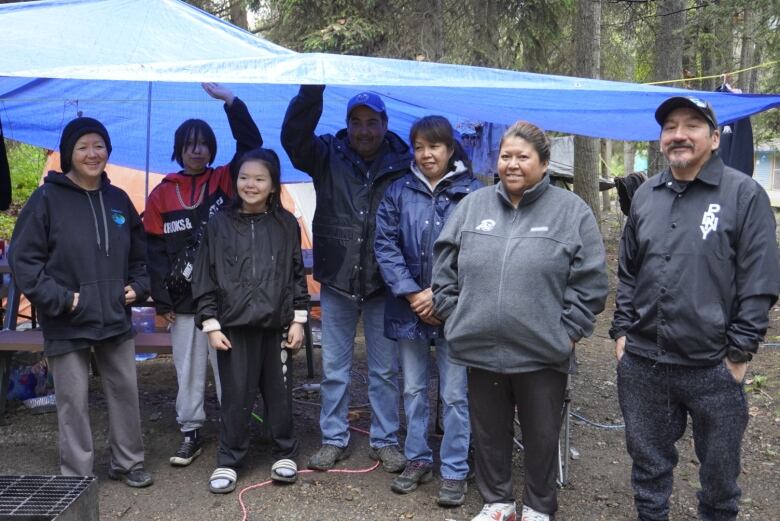 Group stands together under blue tarp.