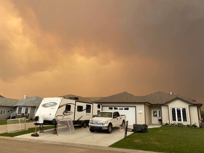 Dark orange and grey smoky skies over a house with a white truck and an RV in the driveway.