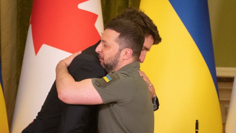 Two men embrace in front of Canadian and Ukrainian flags.