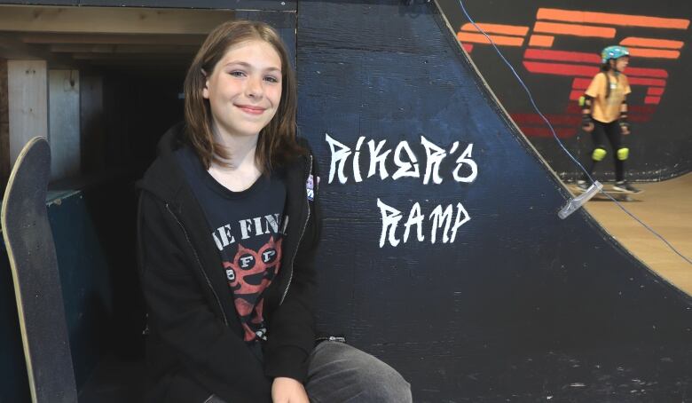 A girl sits beside a skateboarding ramp.