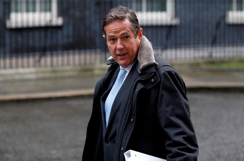 A man in a winter coat and wearing a tie underneath is shown in an outdoor photo.