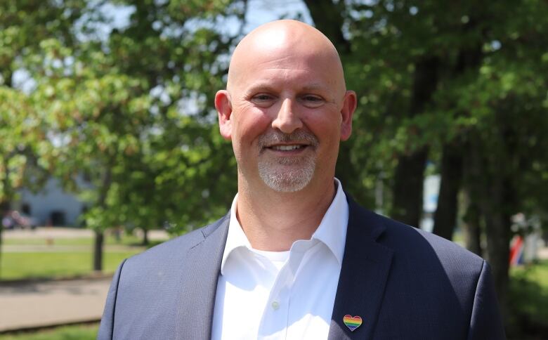 A bald man in a blazer and white button-up shirt smiling.