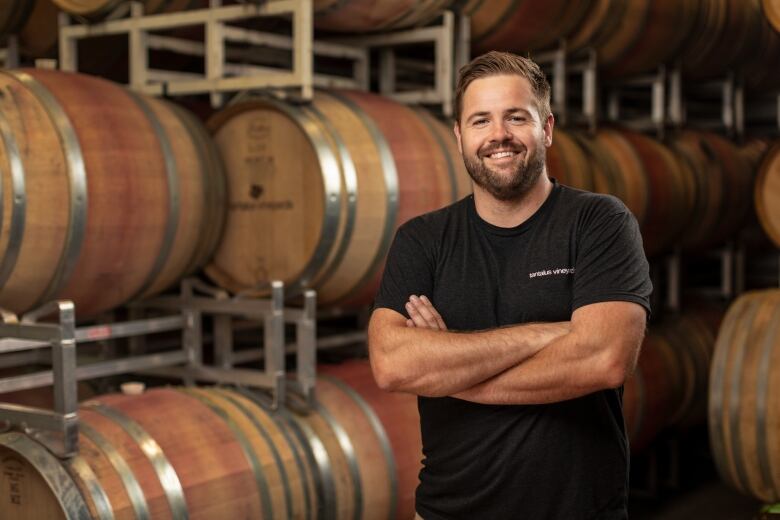 A man stands inside a store room with large barrels of wine in the background.