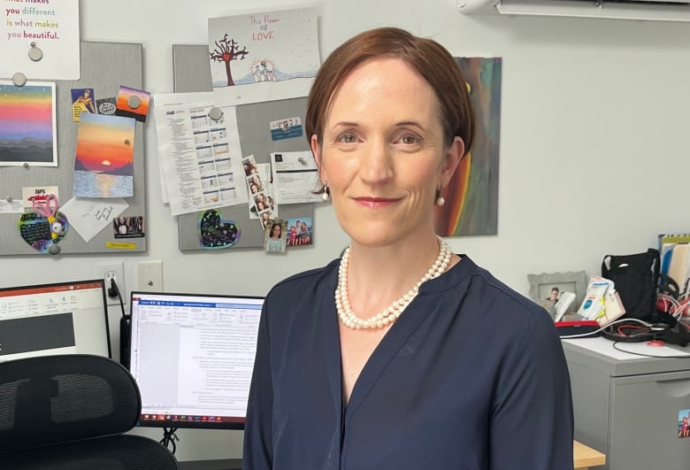 A woman in a business suit stands in front of a desk in an office.