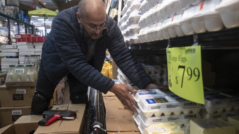 A man stocks carton of eggs on a store shelf.