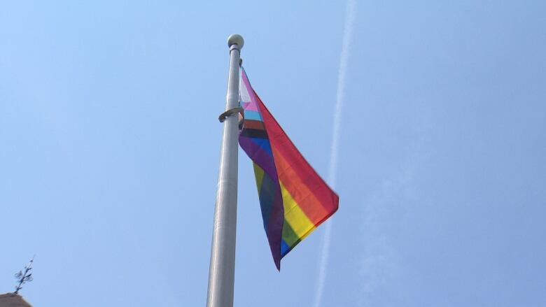 A multicoloured flag flies atop a flagpole against a blue sky.