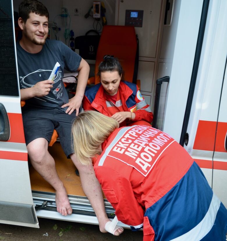 A man sits in an ambulance as his feet are bandaged.