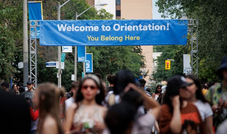 Students walking outdoors, photographed out-of-focus, below a banner that reads 'Welcome to Orientation! You Belong Here.'