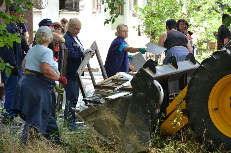 People pile debris into the bucket of a front end loader.