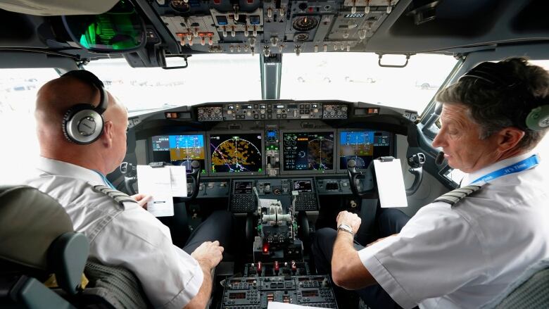 Two pilots in uniform are shown seated in the cockpit of an airplane.