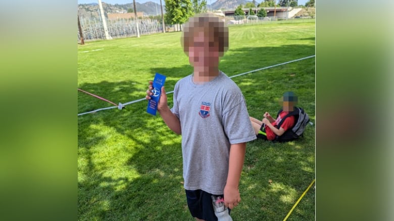 A child with blurred face and in sportswear is pictured standing in a stadium field.