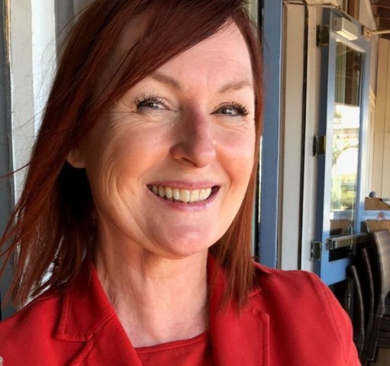 Woman with dark red hair and red outfit smiles at the camera.