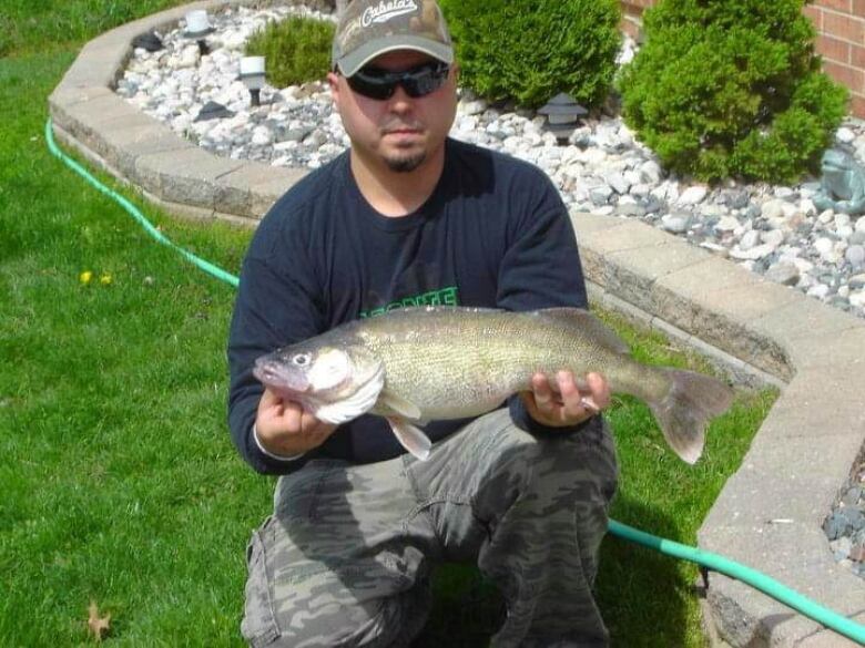 A man poses with a fish on a lawn