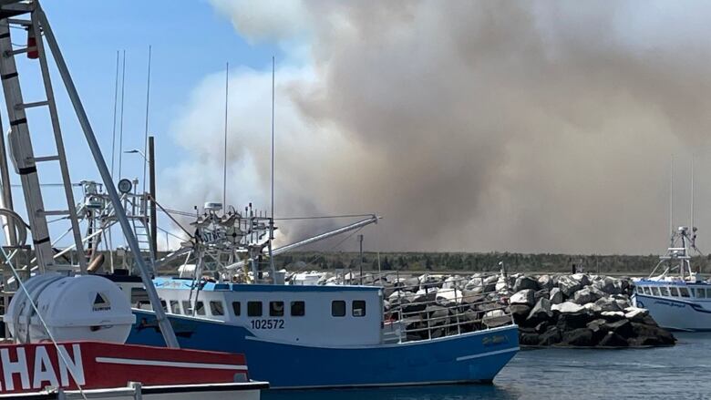 Fishing boats in the water with smoke looming in the distance behind.