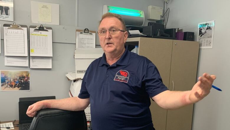 A man wearing a blue polo shirt stands in an office.