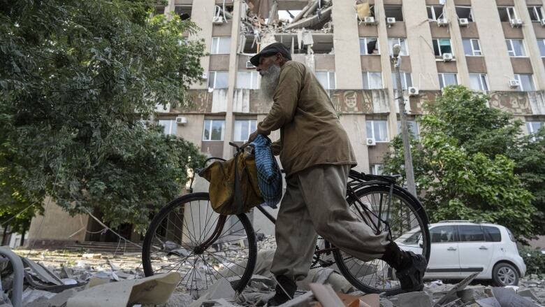 Man pushes a bicycle past front of building in Kherson, Ukraine, which was heavily damaged in a Russian airstrike.