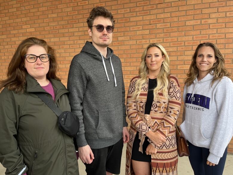 Four people stand together with a brick wall behind them