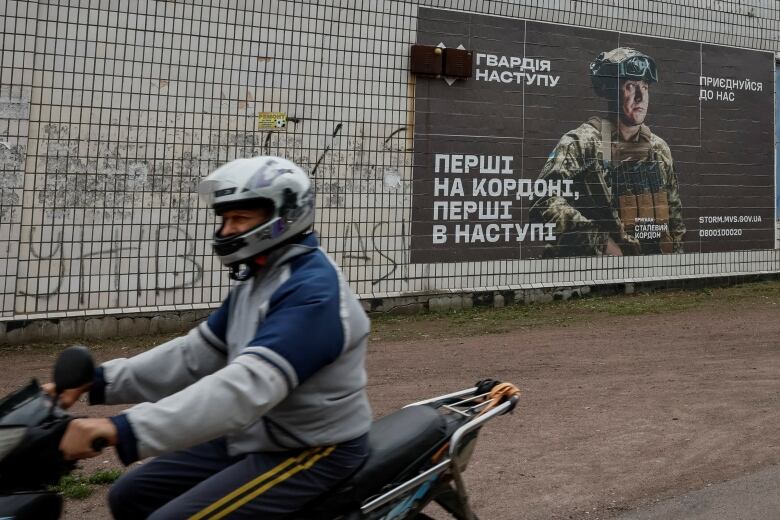 A person rides past a recruitment poster for the Ukrainian army in Hrushivka, Ukraine.