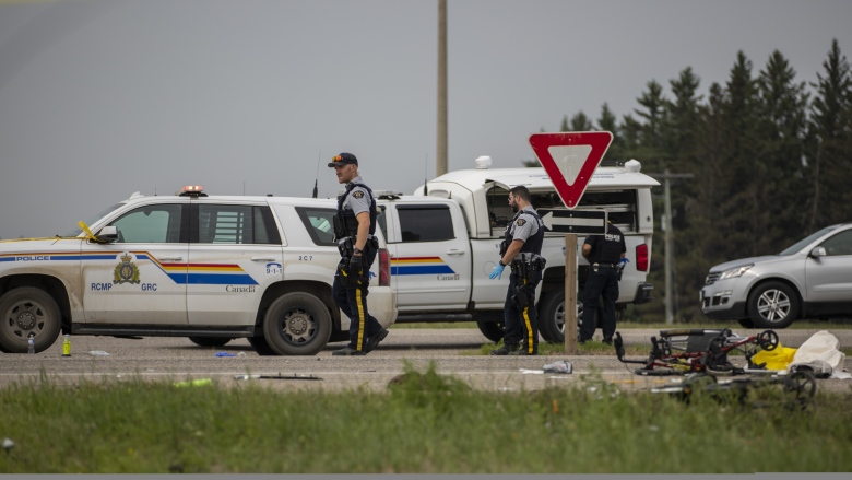 RCMP officers walk along a highway. RCMP cars are parked along the road.