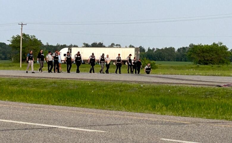 RCMP officers walk in a line along a highway.