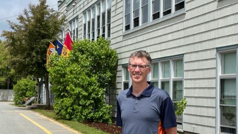 A man with glasses stands outside a school.