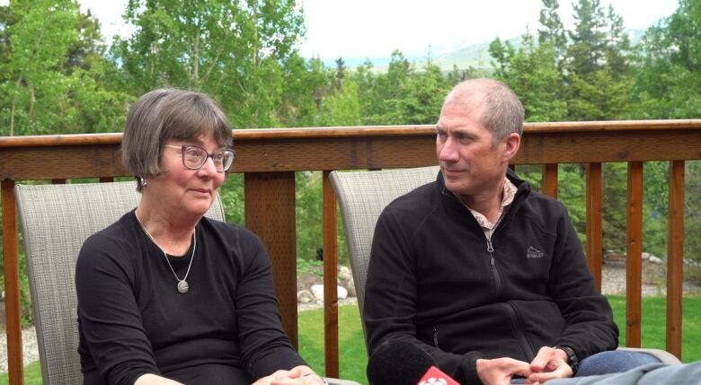 A man and a woman are both wearing black clothing while sitting down.