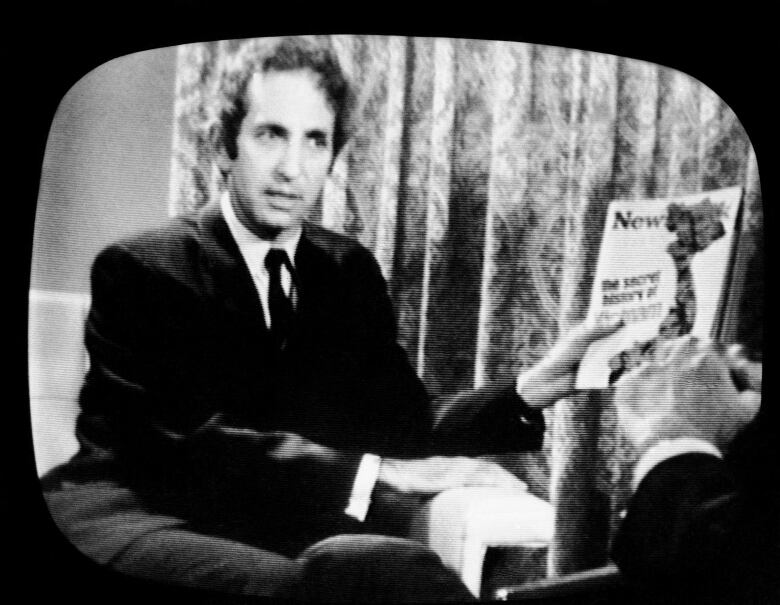 A person is seen holding up a magazine on a black and white TV screen.