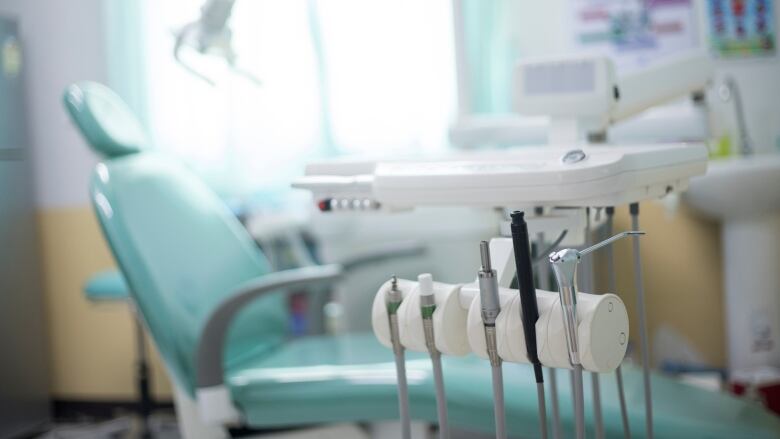 A stock photo shows dental instruments in the foreground with a light blue dentist's chair in a blurred background.