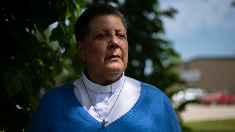 A woman in a white shirt and blue sweater looks at a distance 