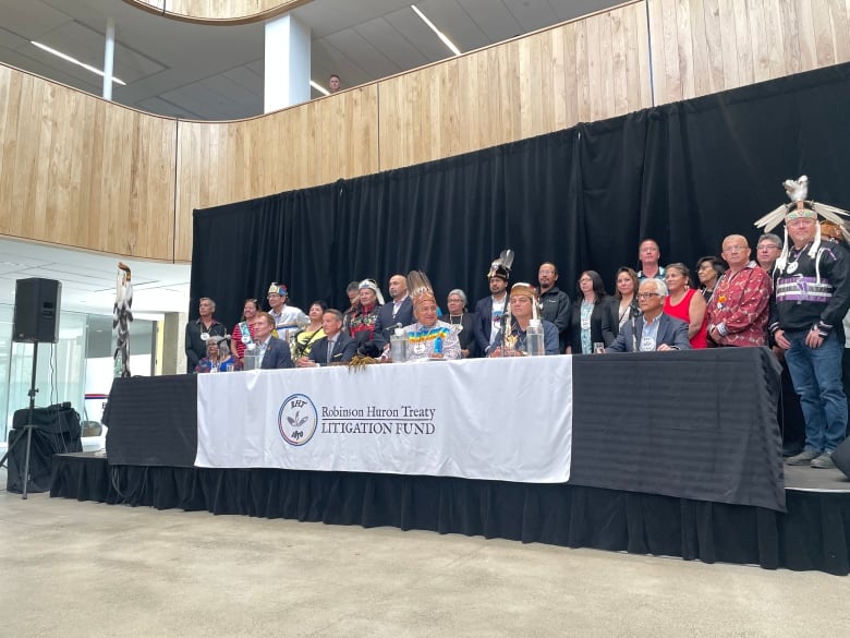 People sitting at a table, some are wearing traditional indigenous regalia.