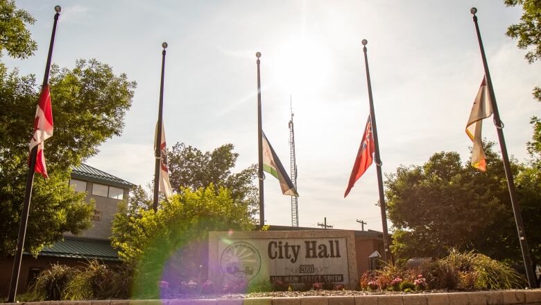 Five flags fly at half mast behind a sign that says 