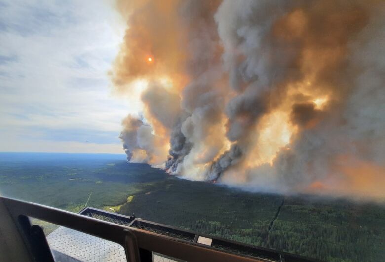 Plumes of orange and grey smoke rise from a large wildfire.