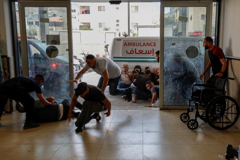 People scramble into the entrance of a hospital while others take cover behind and ambulance.